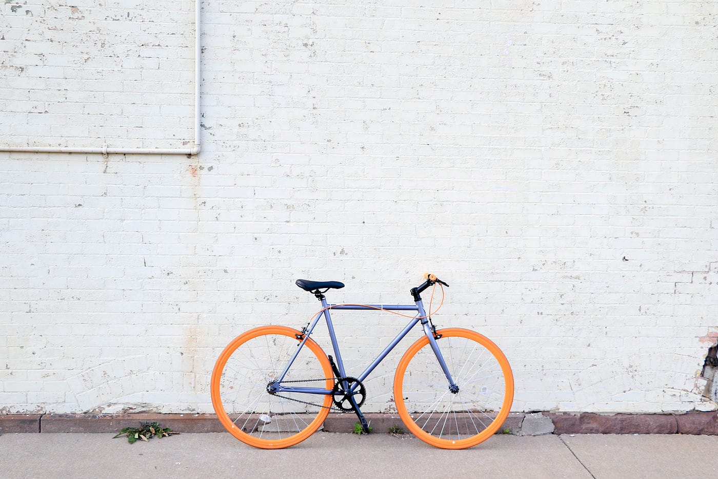 A bicycle, with yellow tire and a blue frame, sits in front of an old-appearing white wall.