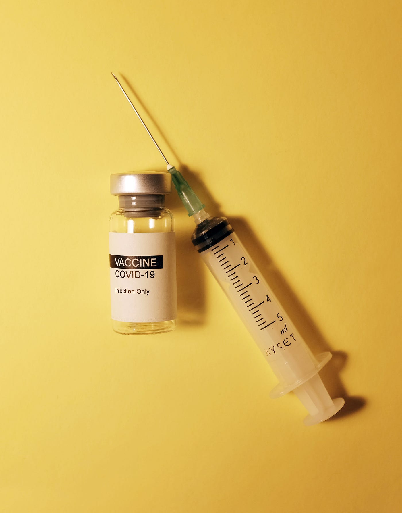 Covid vaccine vial on the left; empty syringe on the right. Yellow background.