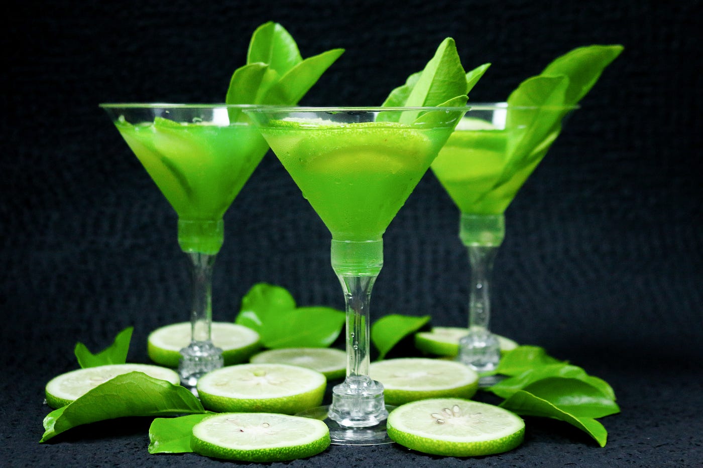 3 lime drinks in champagne style glasses lined up against a dark background.