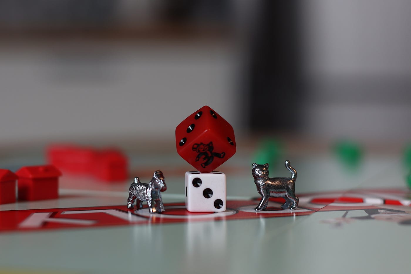 Monopoly game pieces, including a white dice in the center of the image (and a diagonal red dice balanced on it). There is a small silver dog to the left of the die and a silver cat to the right of it. All sit on a board with the word “Monopoly” partially visualized. Leisure activities are associated with a lower risk of dementia, according to a new large review.