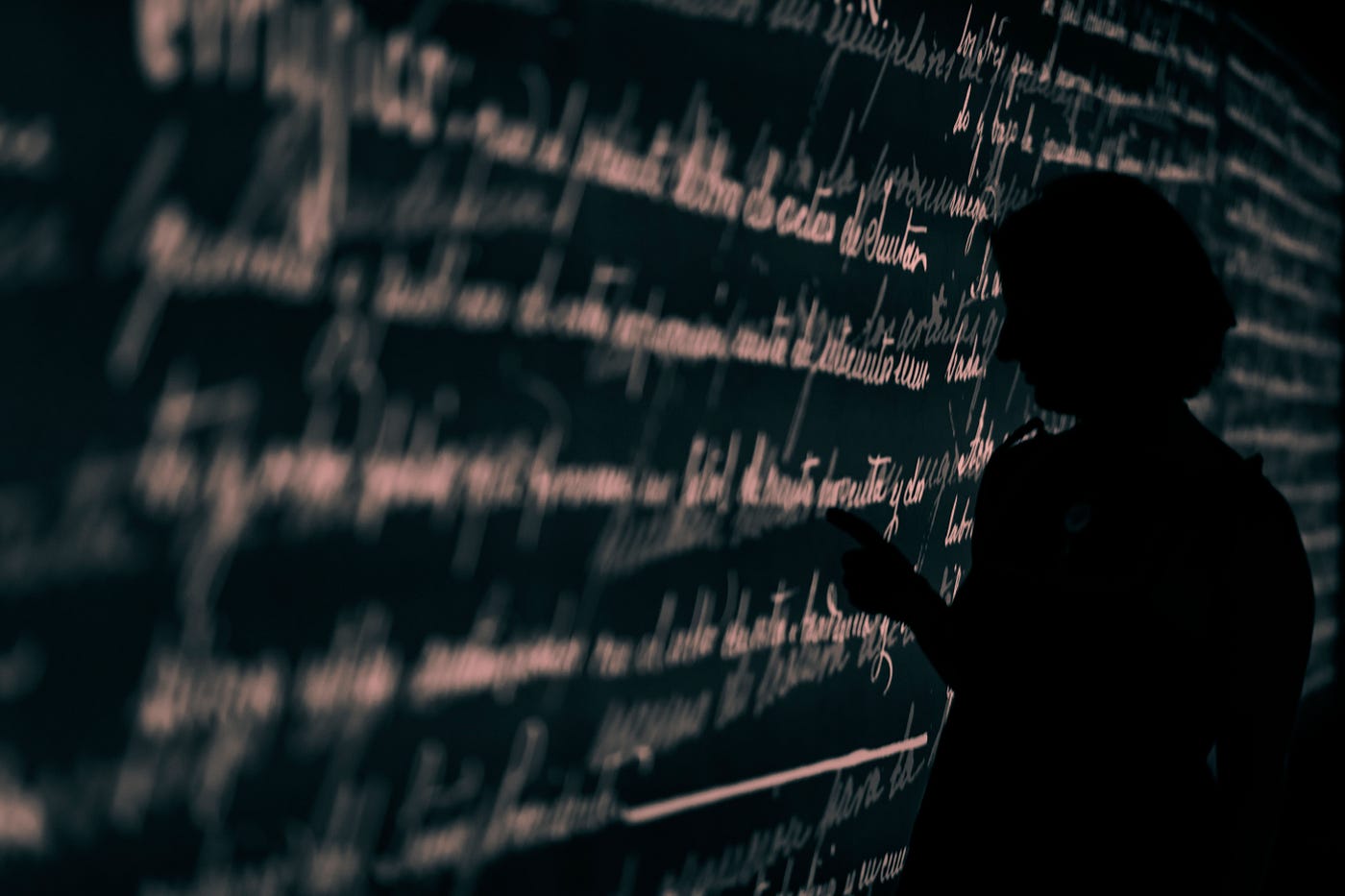 Blurred cursive (in a foreign language) on a black board, written in white letters.