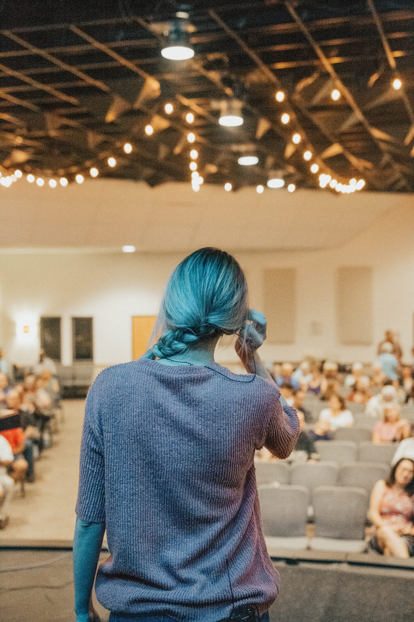 Photo of a woman from behind, who is on a stage adjusting her earpiece in front of an audience.