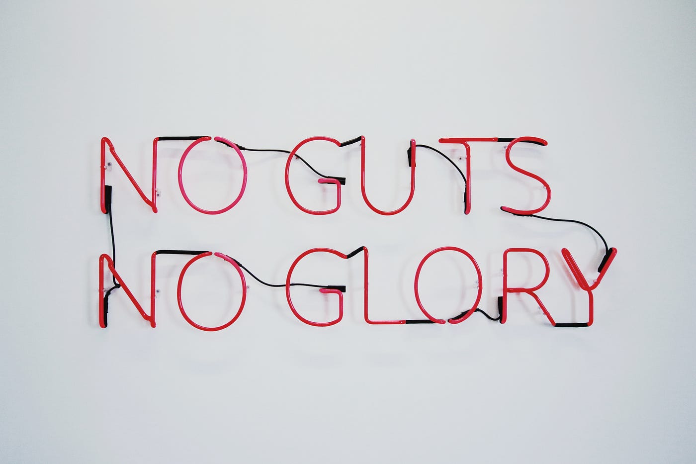A neon sign in red letters that says: NO GUTS NO GLORY on a gray background.