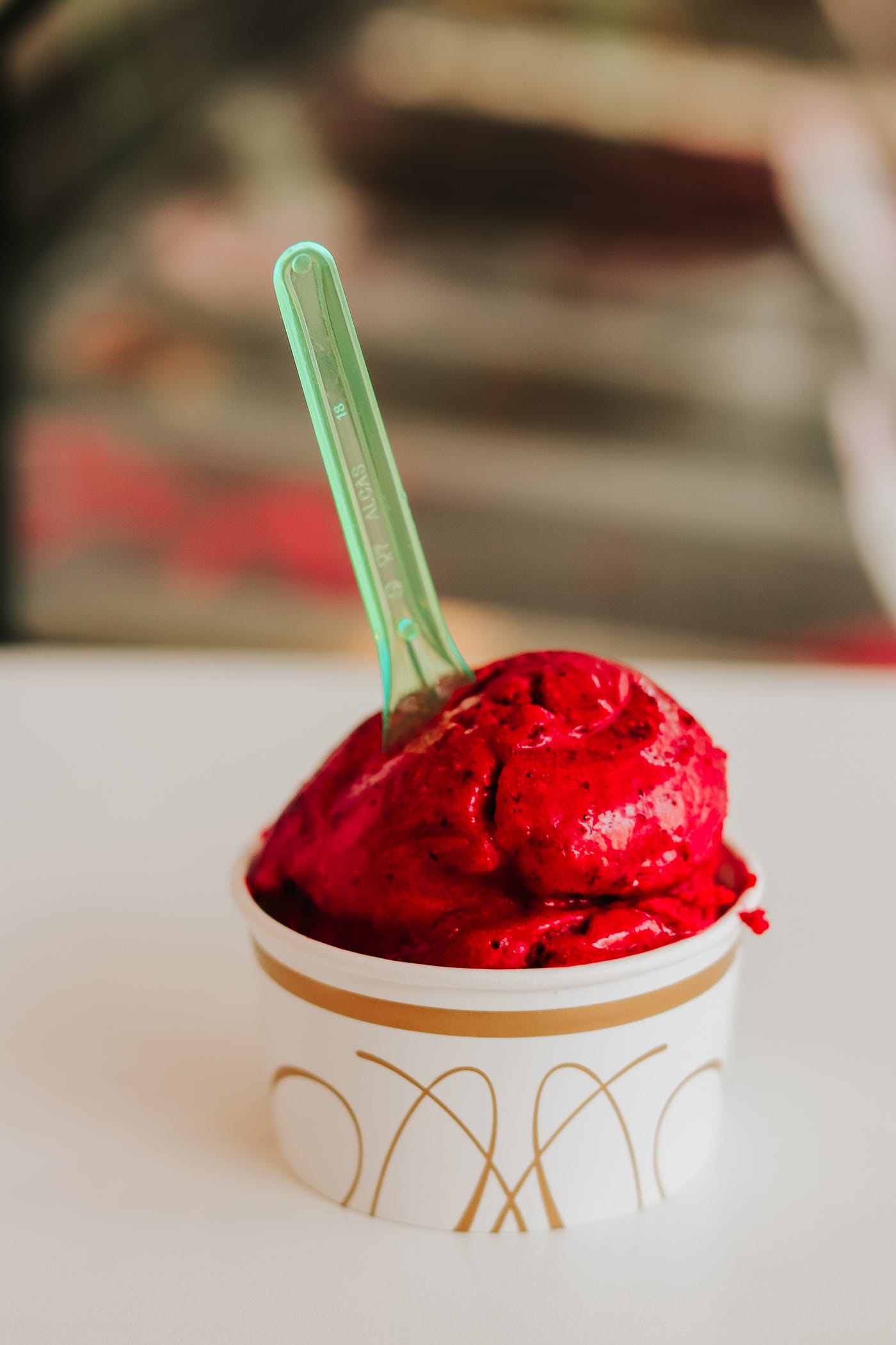 Red sorbet in a cup with a green spoon.
