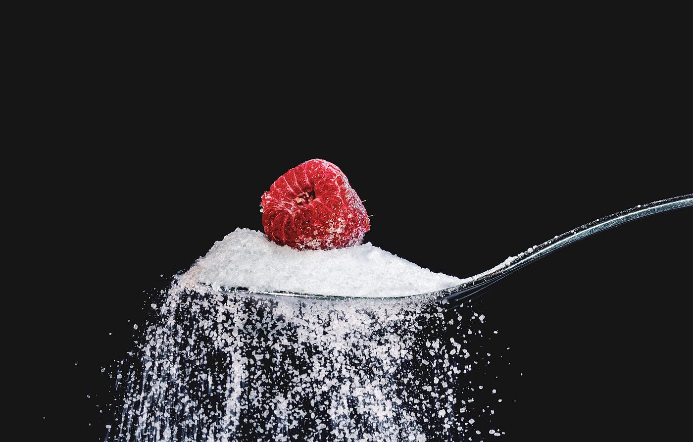 A spoon emerges from the right, filled with sugar spilling over the edge. The sugar has a raspberry perched on top of it. Black background. Exercise can help with type 2 diabetes.