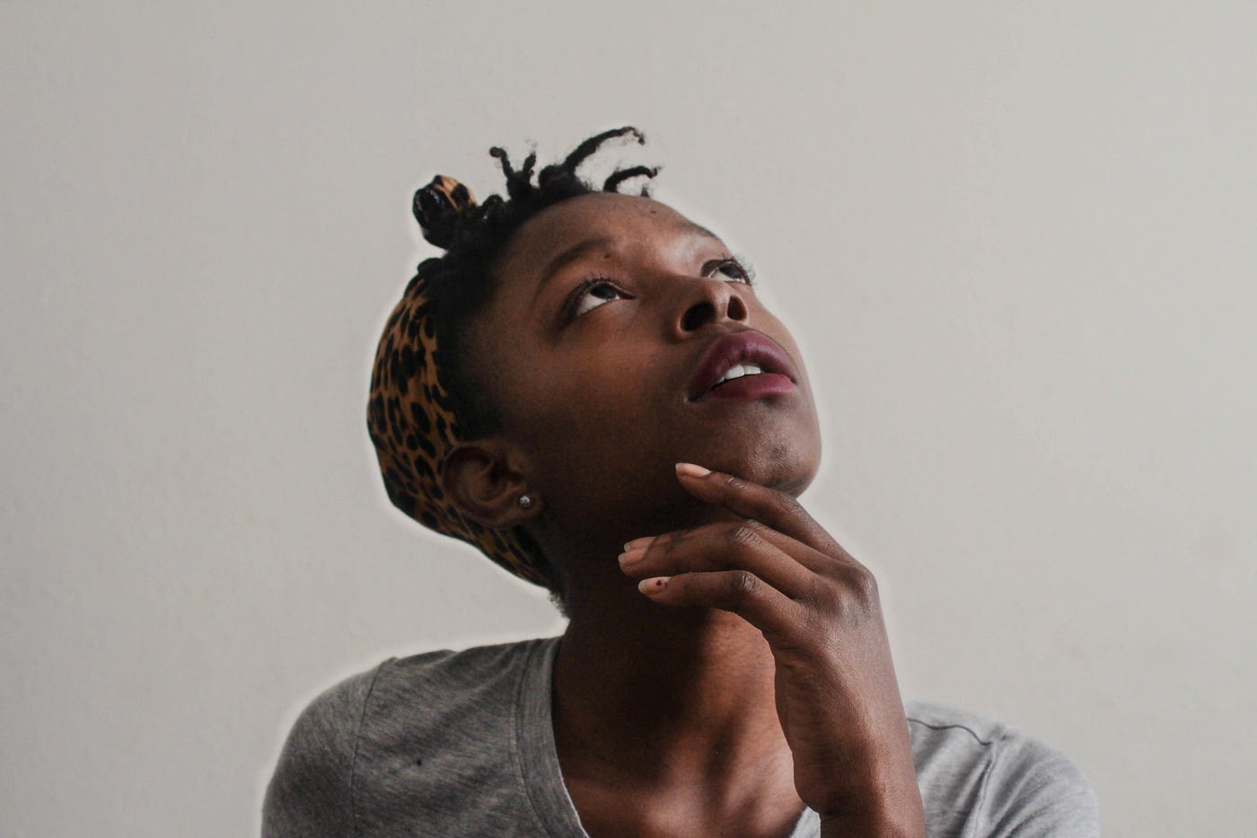 Black woman looks skyward, her hands clasped under her chin. She wears a gray shirt.
