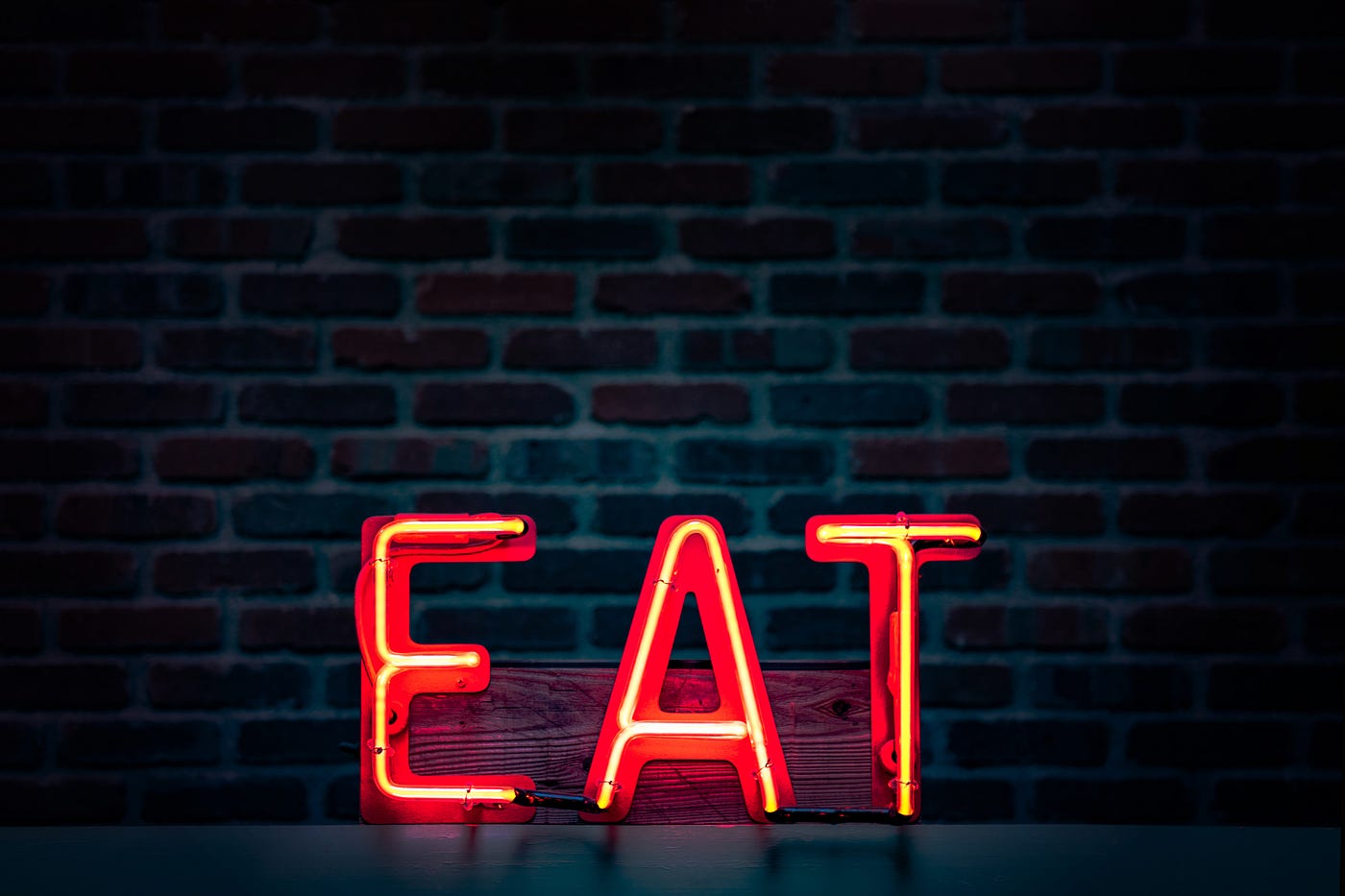 Red neon sign says “EAT” with a brick wall in the background. Inadequate sleep can lead to weight gain.