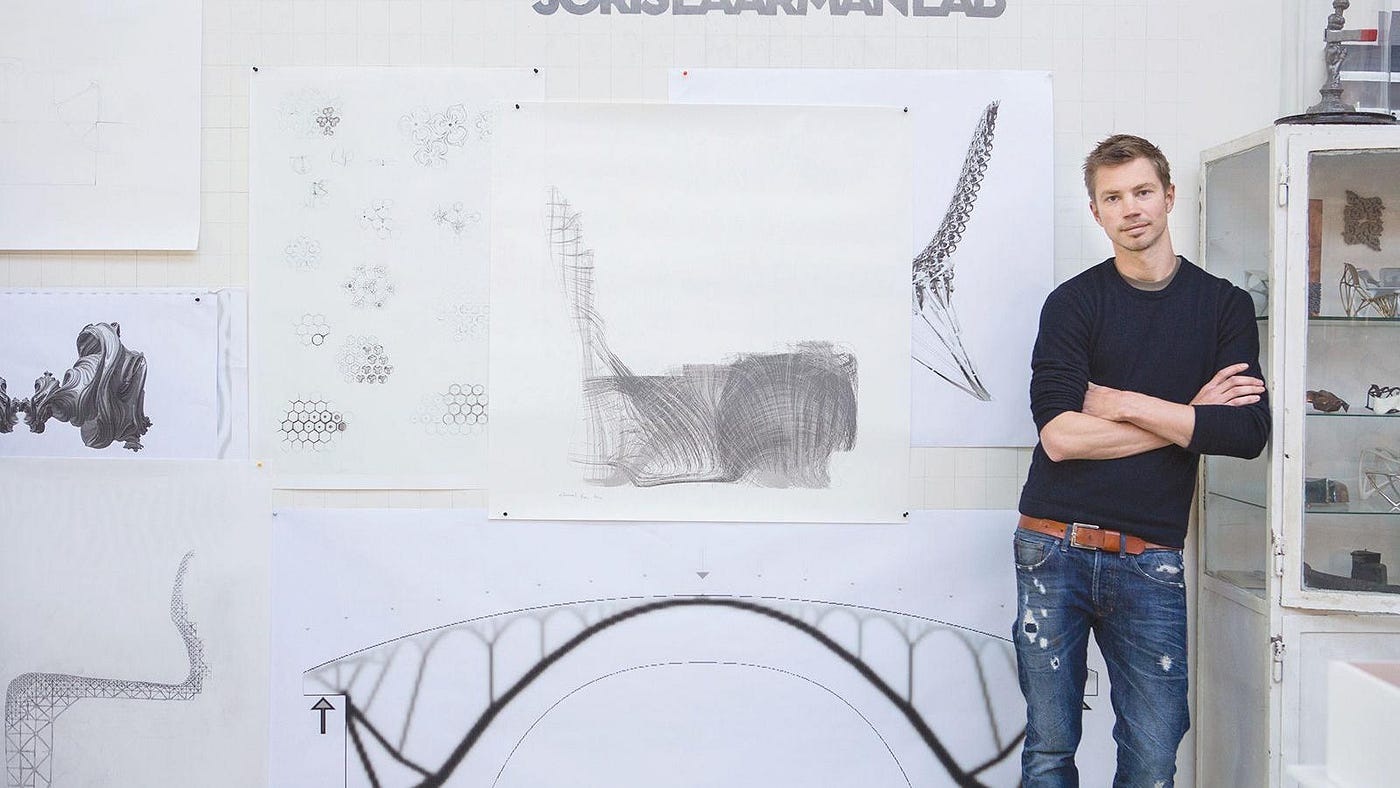 Joris Laarman stands with his arms folded against a wall of sketches and inspiration under a sign that reads “Joris Laarman Lab.”