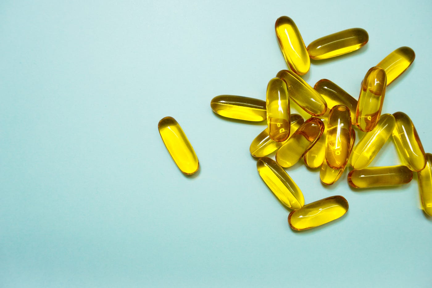 About a dozen and a half elongated capsules, yellow in color, sit haphazardly on the right side of the screen. Powder blue background. Vitamin D appears to slow aging among African Americans deficient in the vitamin.