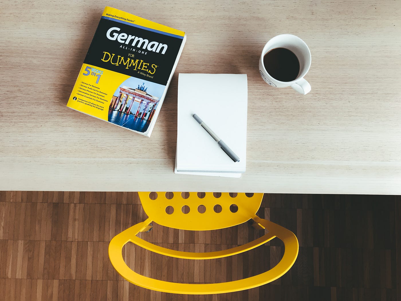 A language learning book on a desk with an empty pad of paper and coffee.