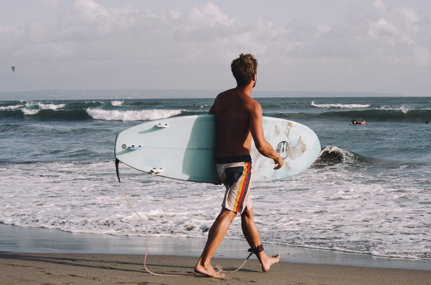 A picture showing a young boy wearing shorts and carrying a surfboard in Australia