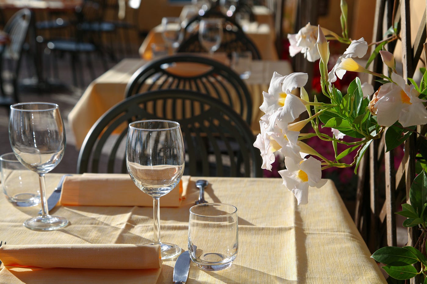 A closeup of a table, laid out for dinner. Table has a flower arrangement, and is on an outdoor patio.