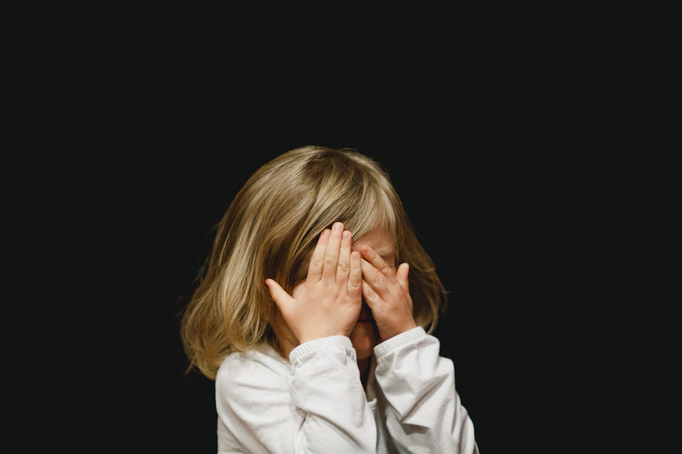 Little girl covering her eyes feeling sorry, in front of a black background