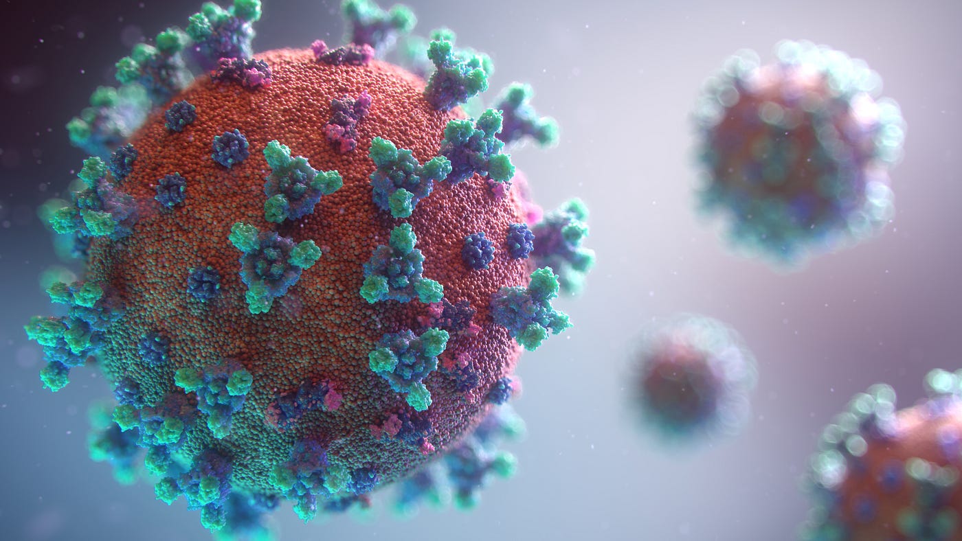 COVID-19 vaccine particles float against a gray/white background. The virus has numerous small blue and green appendages, with the virus spere itself red and textured.