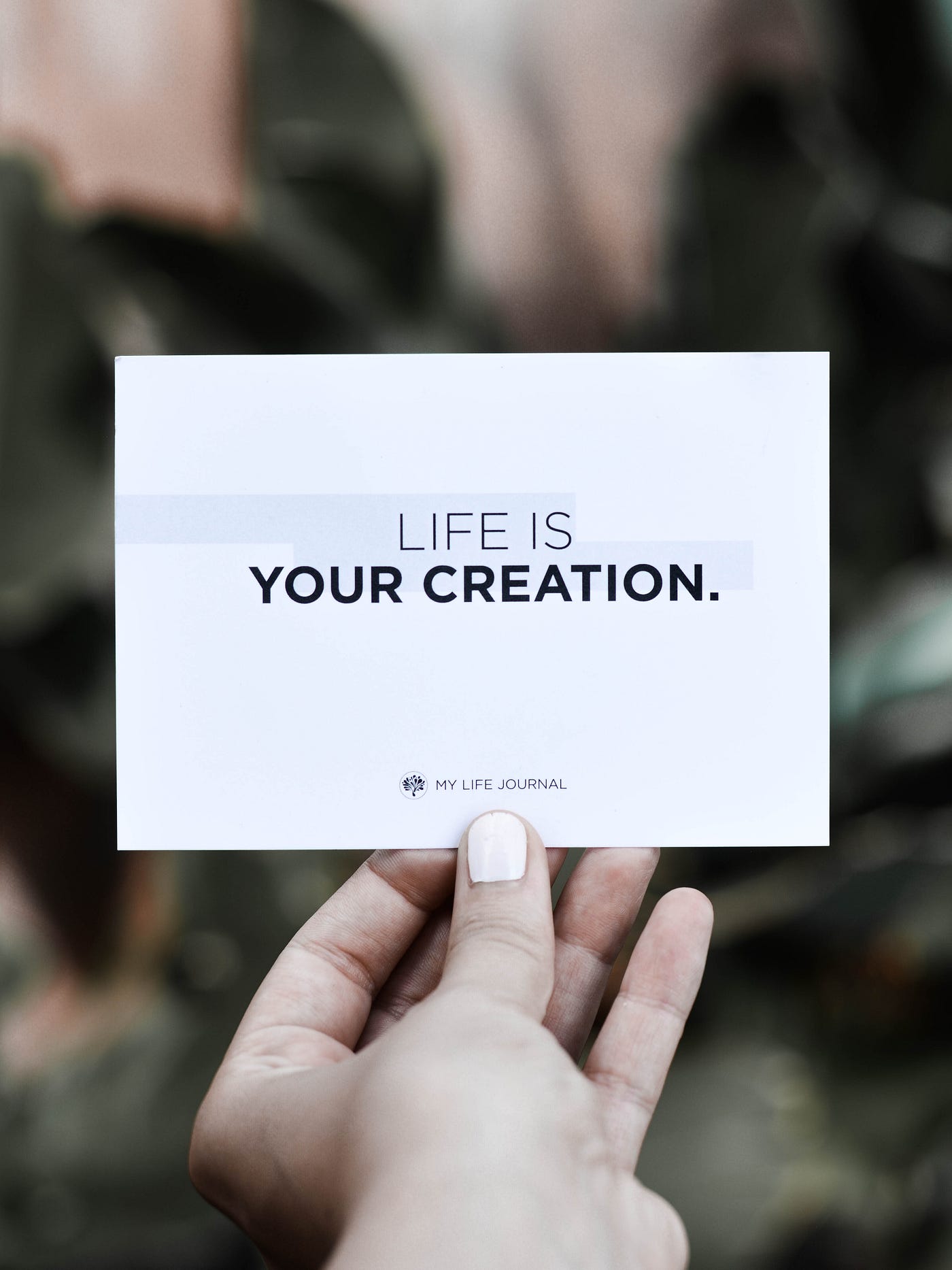 A picture of a woman’s hand holding a white card that reads: “Life is your creation.”