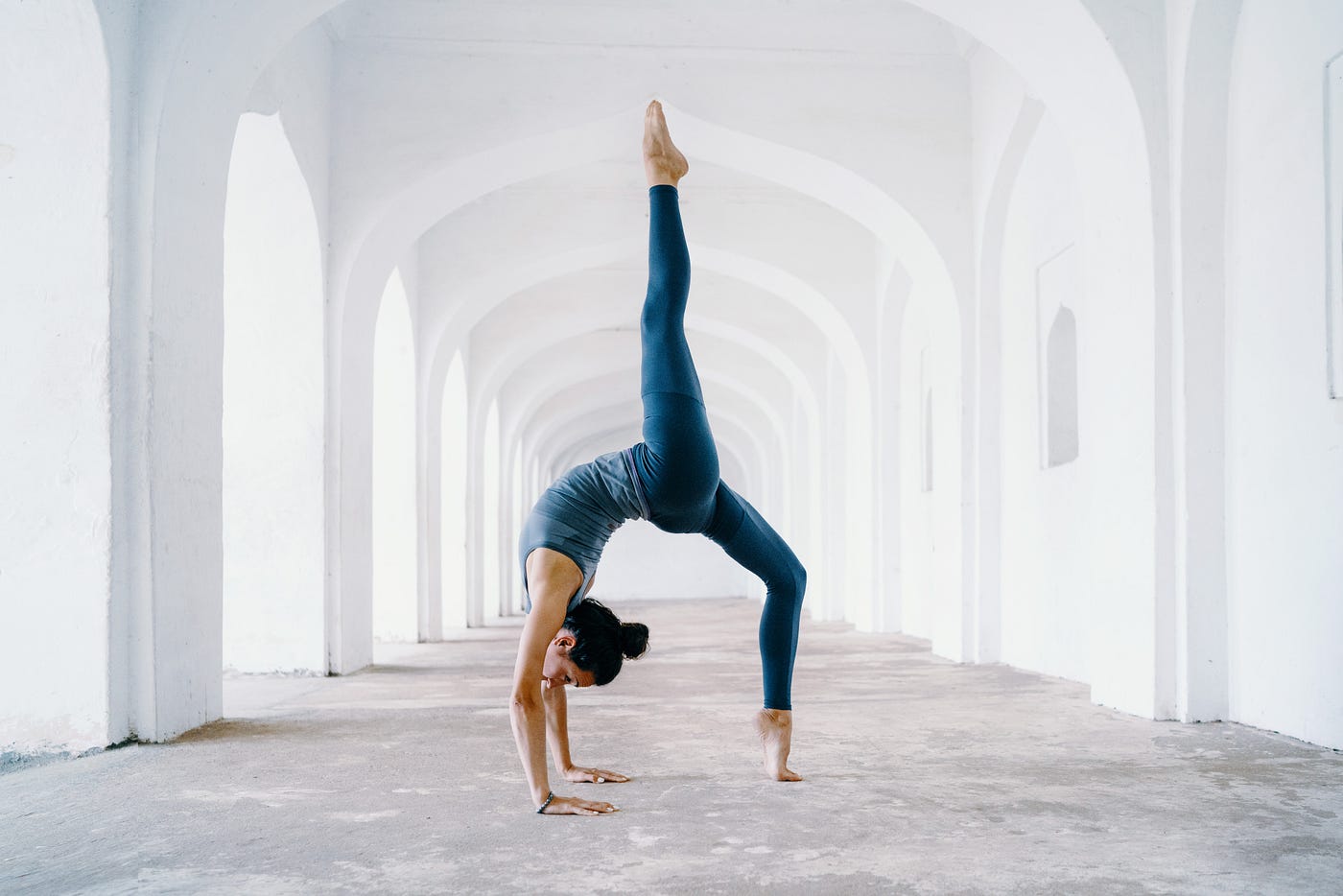 Woman performs yoga. One leg points to the ceiling as the other is en point on the ground.