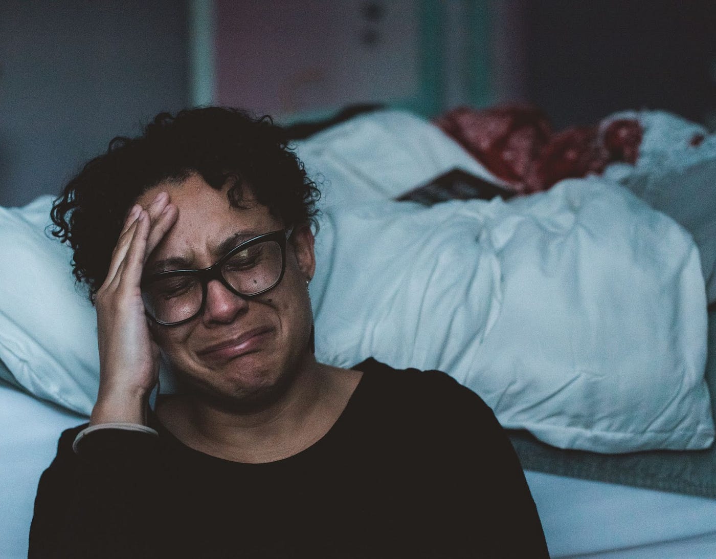 A woman crying while sitting on the floor besides bed.