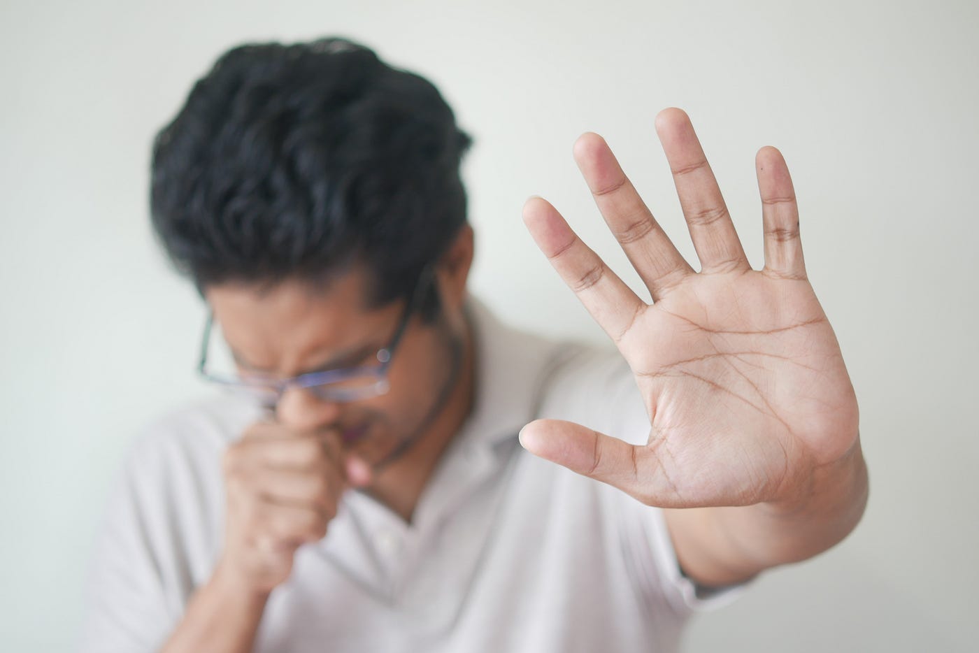 A male extends his open left hands to the camera as he coughs into his fist.