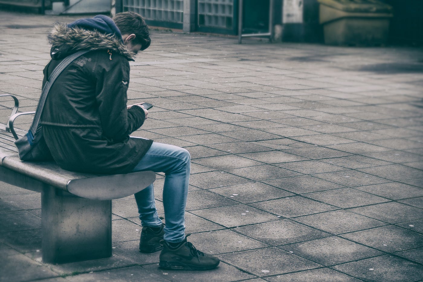 The Toxic Office: How to Deal With a Bully Boss. Someone sits on an outdoor public bench, keenly looking at their mobile phone.