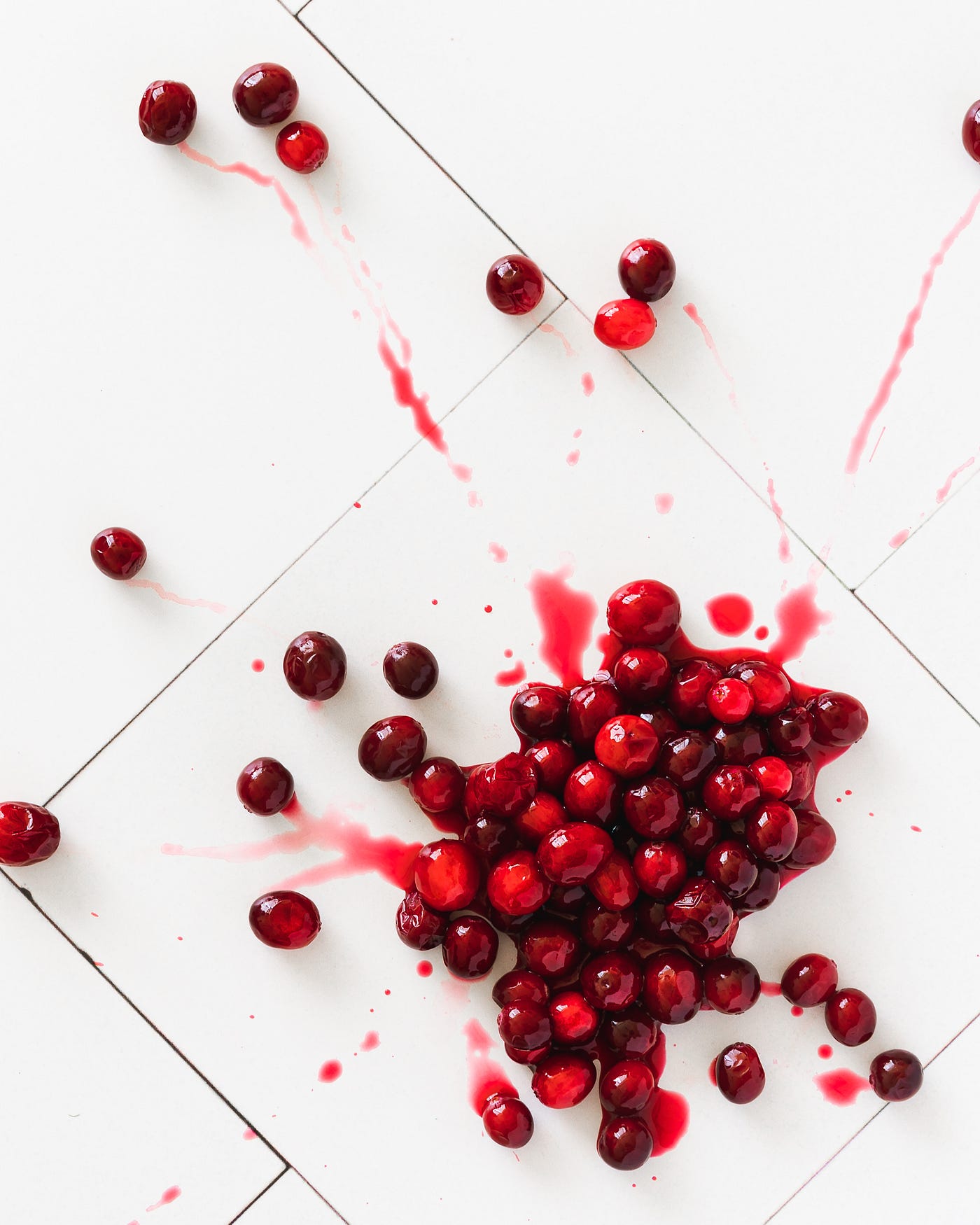 A bunch of deep red cranberries drops from above, splashing on a white floor.