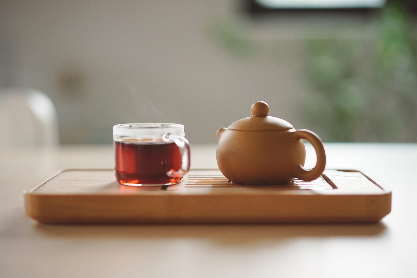 Tea in a clear cup on the left. A tan teapot perches on the right Both sit on a wooden stand. Preferences for black tea are influenced by genes.