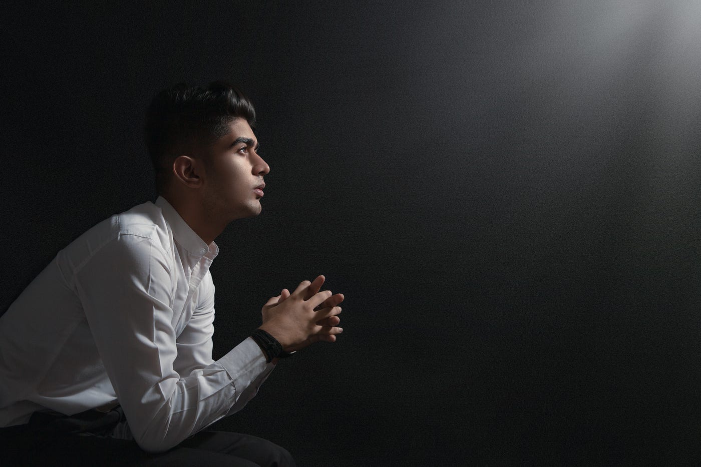 A young man in a white shirt praying.