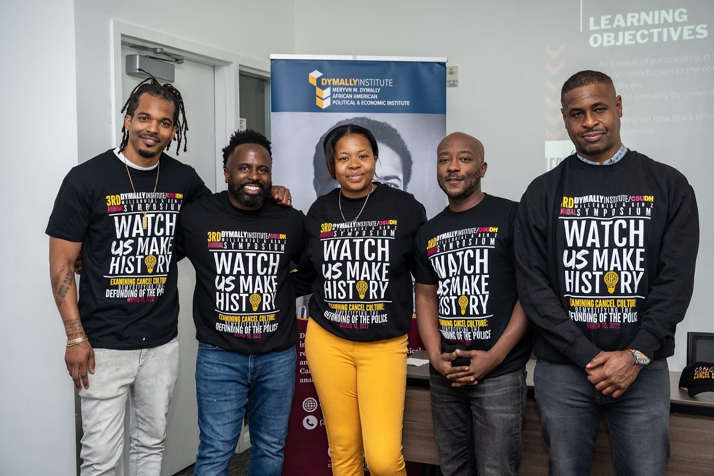 Picture of five African American leaders wearing Watch Us Make History Shirts. Left to Right: Ande Spicer — Entrepreneur & Community Activist, Jarrod D. Benjamin, MBA — CEO, The Lead Firm, Jasmine Gates — Founder, New Black History Maker, Brandon Mims — Treasurer, City of Compton, and Anthony Onwuegbuzia — Mervyn M. Dymally African American Political & Economic Institute.