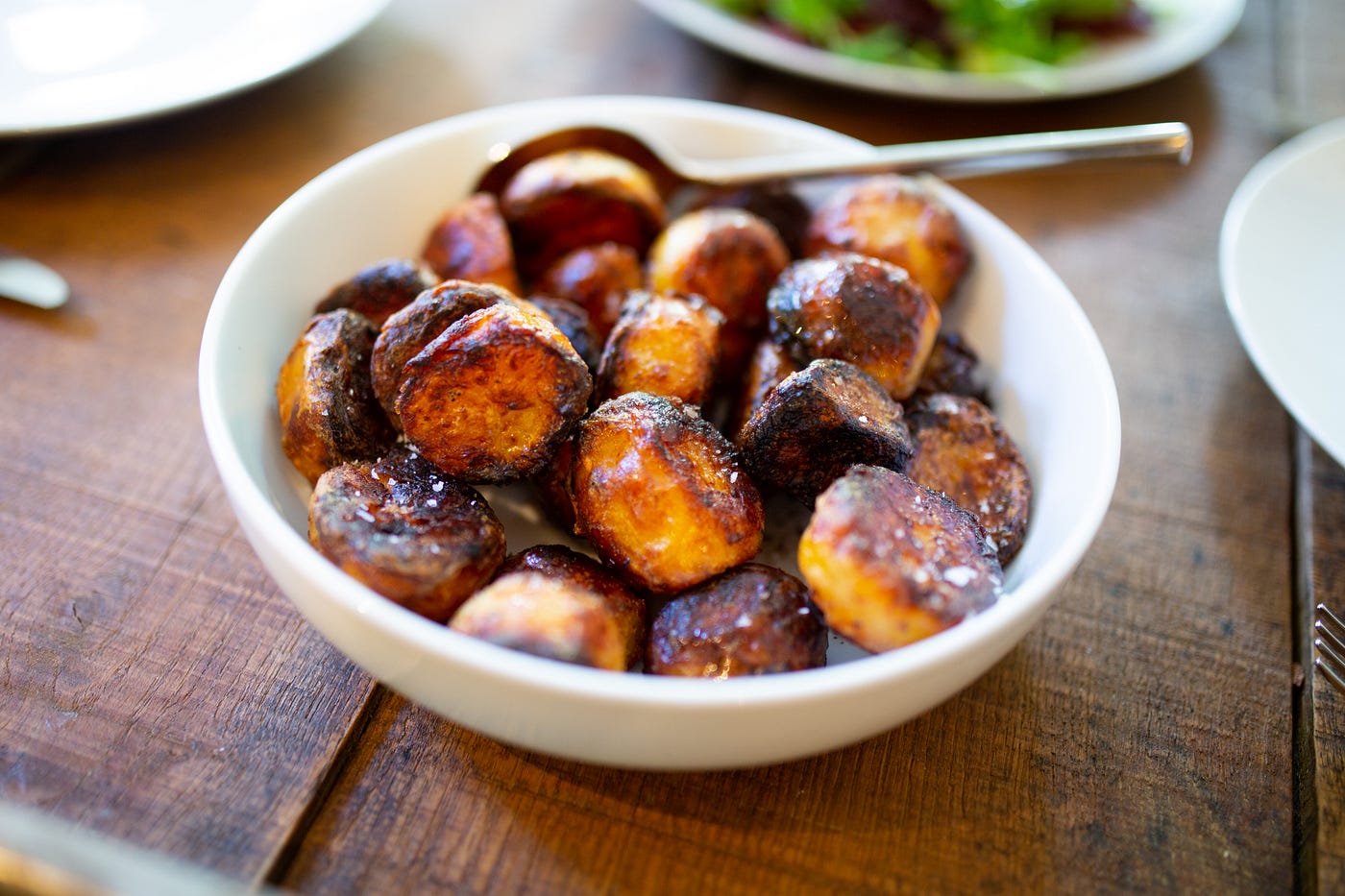 A white bowl of roasted potatoes sits on a wooden table. A new study shows diets with beans or potatoes both lead to weight loss.