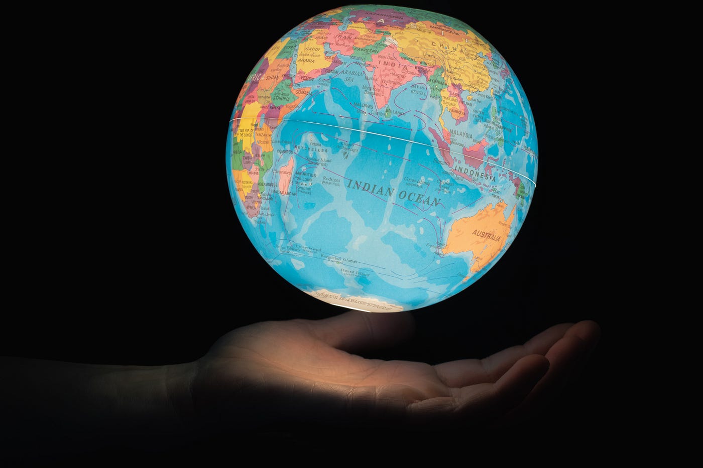 A an outstretched hand emerges from the left side of the image, with an illuminated toy globe floating above it. Black background.