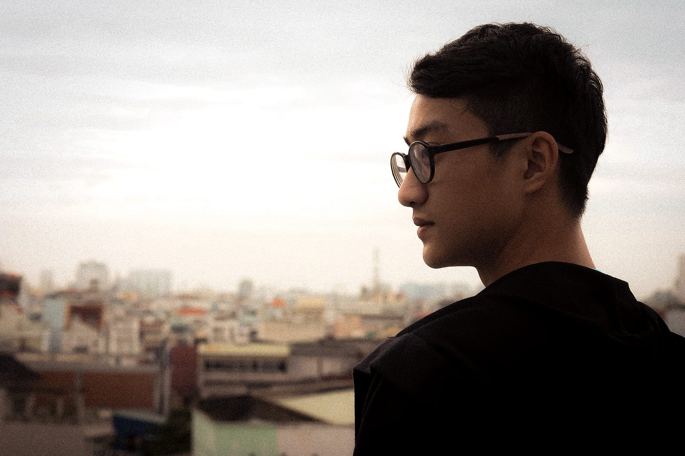 Man with glasses standing on rooftop looking sideways.