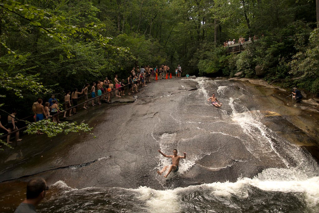 A photo of sliding rock in Asheville, North Carolina with two people sliding down the rock