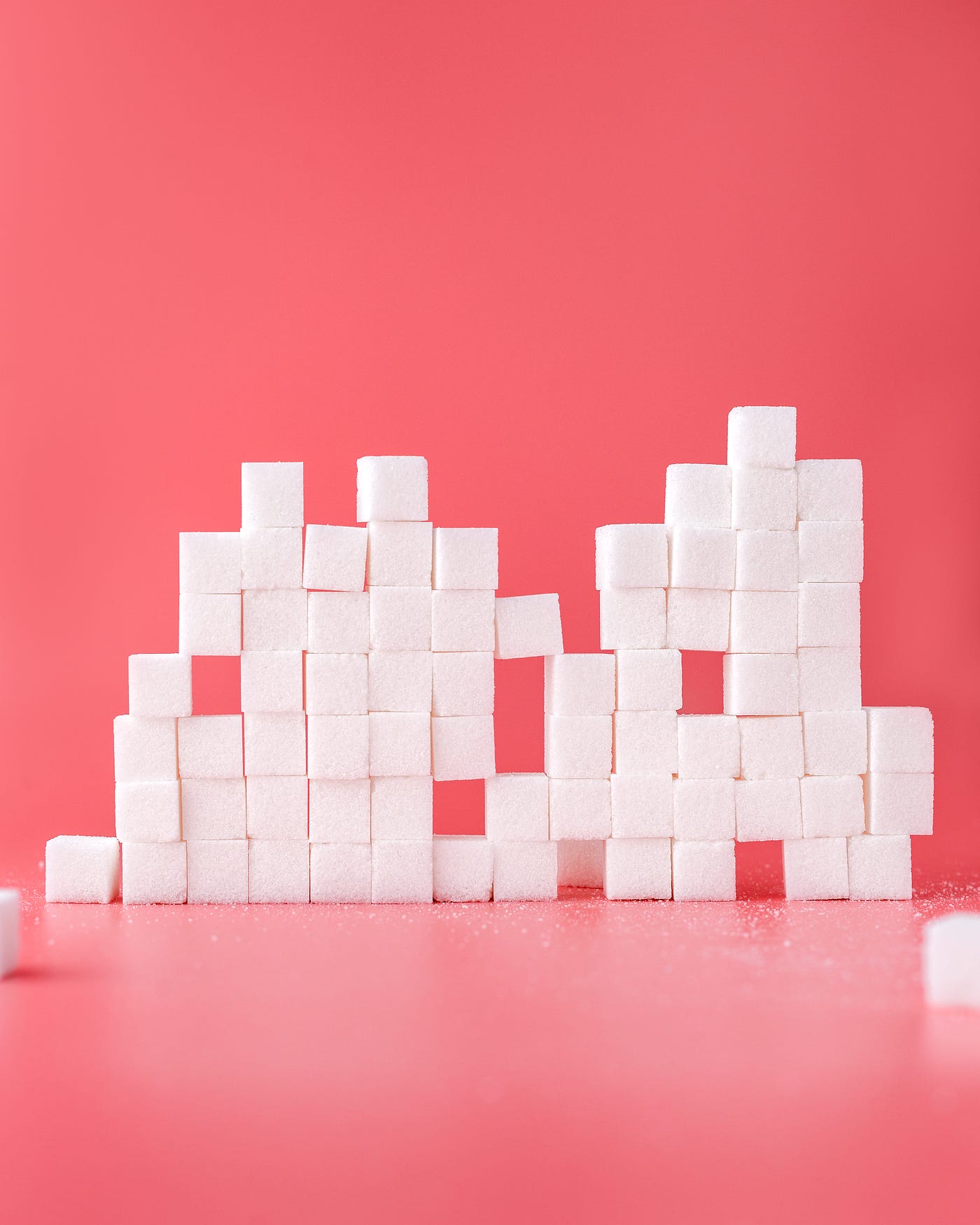 A stack of sugar cubes, numbering about 15 from left to right and seven cubes high. There are missing cubes in several locations. Pinkish background.