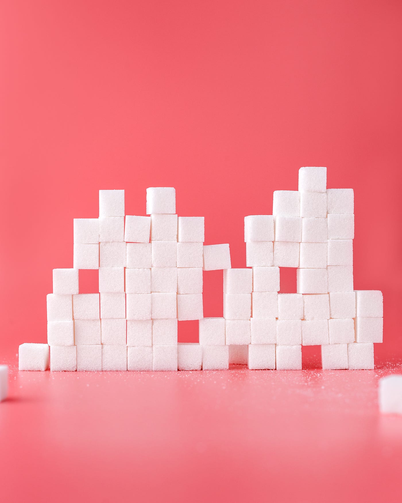 A stack of sugar cubes, numbering about 15 from left to right and seven cubes high. There are missing cubes in several locations. Pinkish background.