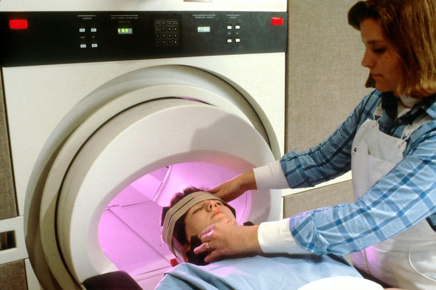 A young white woman is guided (by a technologist) into an magnetic resonance imaging (MRI) machine.