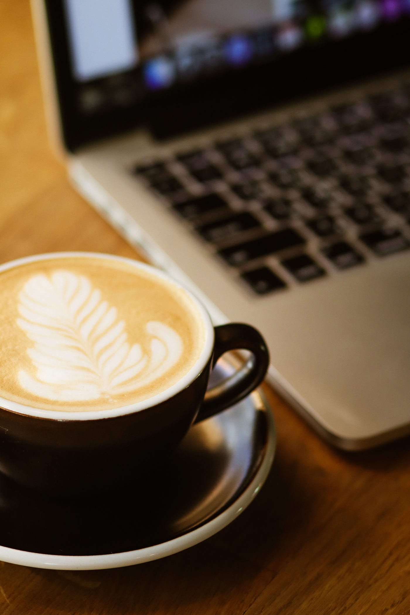 A black ceramic coffee cup with a latte art next to a laptop.
