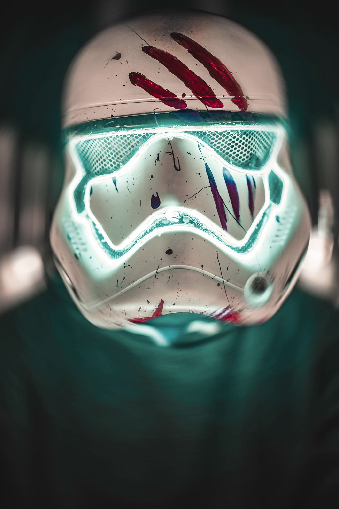 White futuristic full head Storm Trooper helmet glowing with green eye pieces and mouth guard, scratches on the metal and blood smears