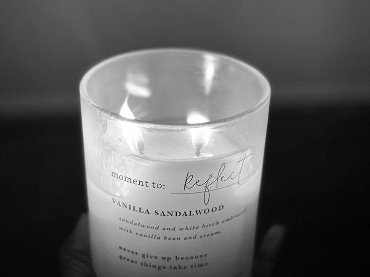 A lit candle with the words “moment to Reflect” written on it