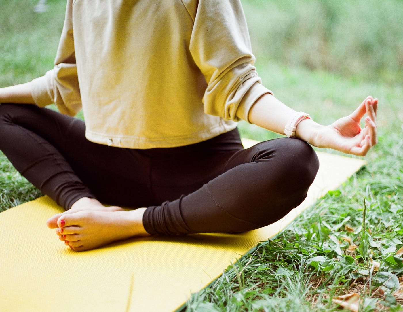 woman sits on yoga mat in grass and meditates