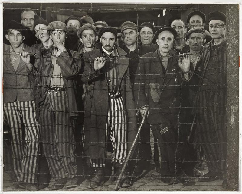 Prisoners in a Nazi concentration camp stand before a barbed-wire fence.