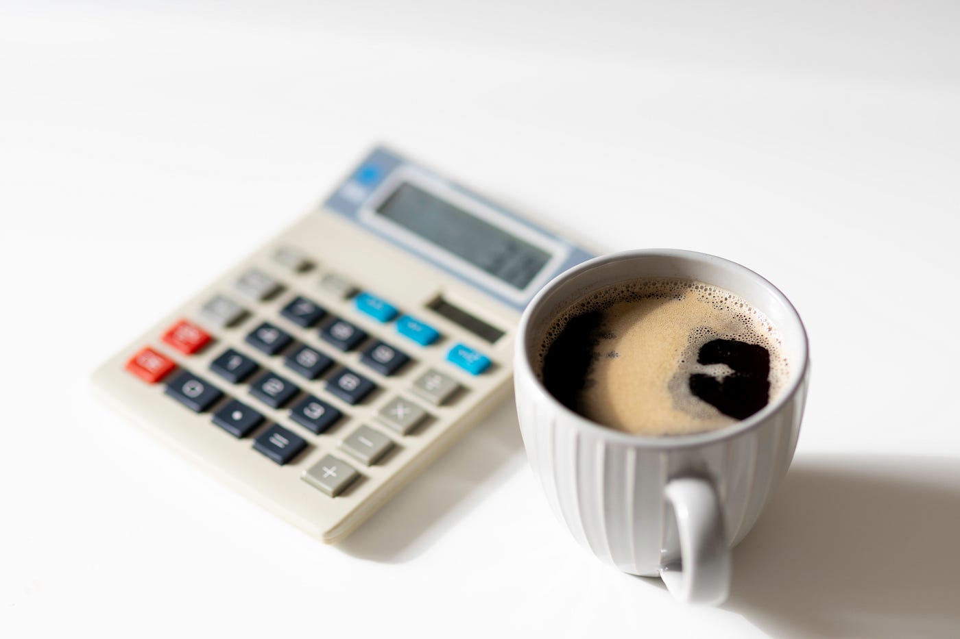 A calculator and a cup of coffee sit side-by-side.