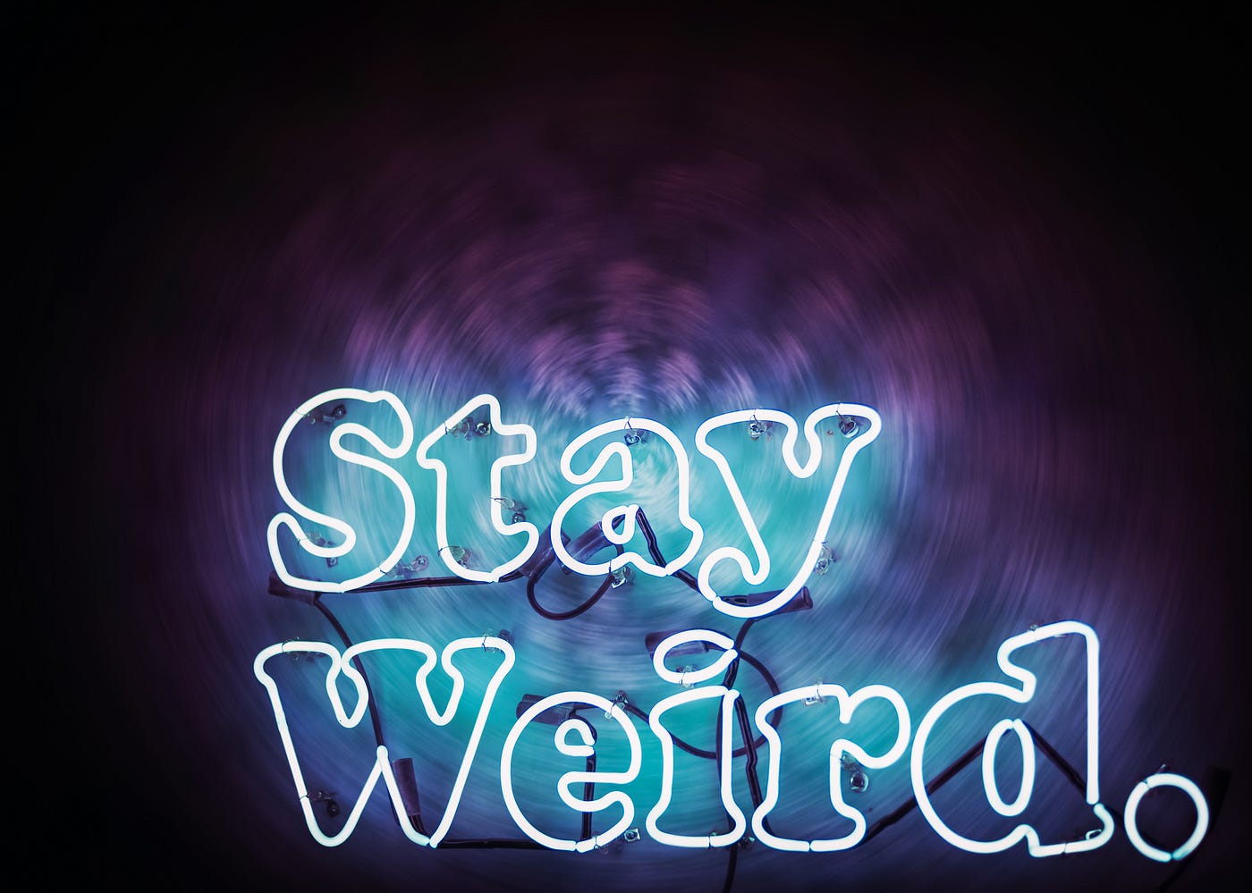 Dark purple & violet background against which the words “stay weird” are contrasted in white-outlined turquoise-blue lettering.