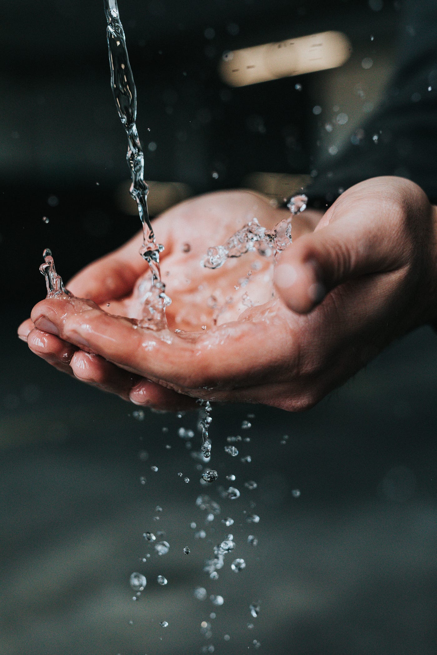 Tow hands are seen in close-up, palms up, as water splashes into them from above.