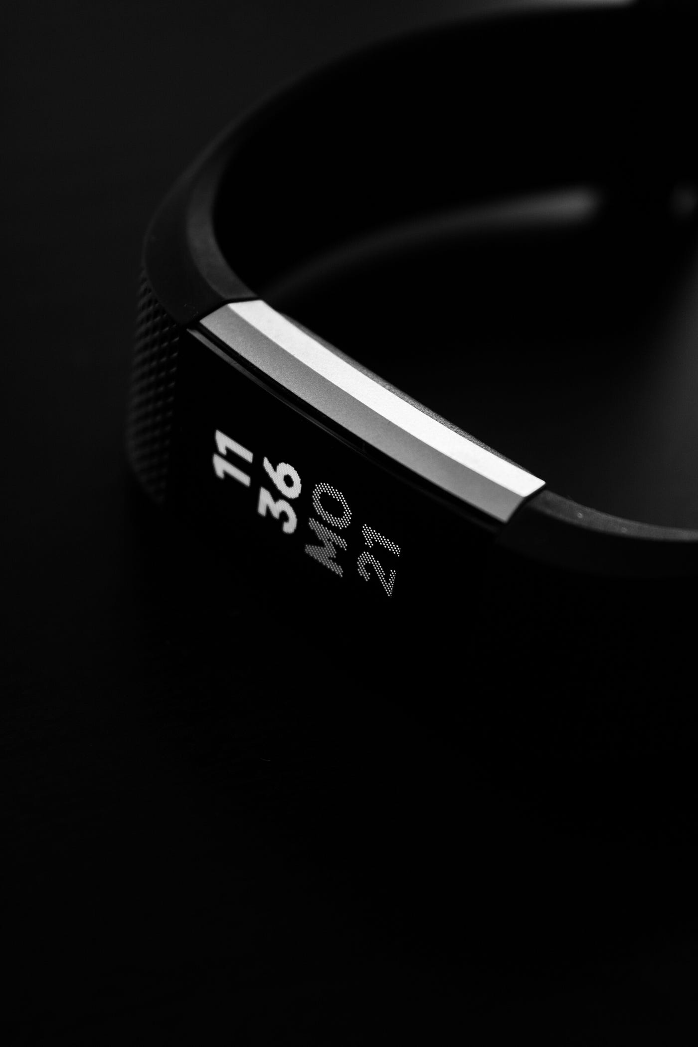 A black Fitbit activity tracker lies diagonally across the image. The device reads 11:36, is black, and has silver edges around the watch part.