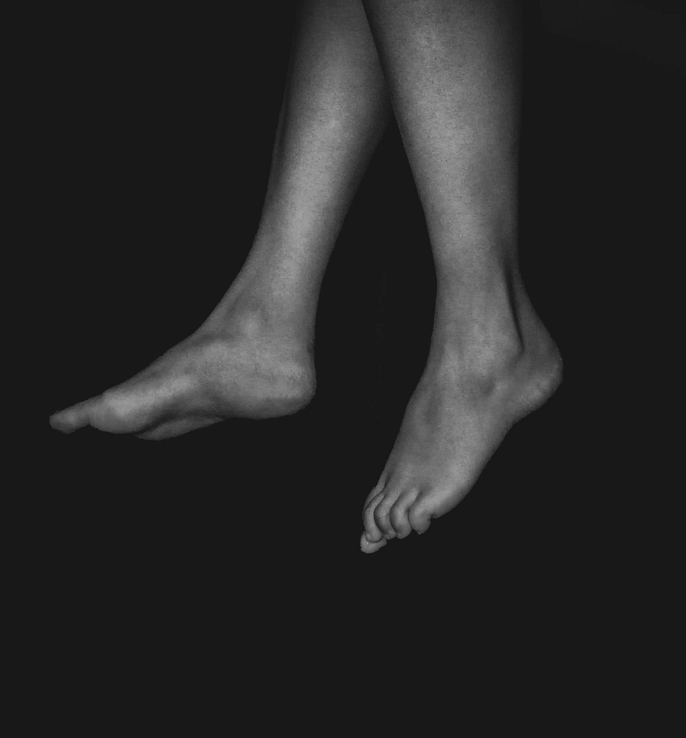 Two legs dangle into the image from above. We see the lower extremities from upper calf level down. Black background.
