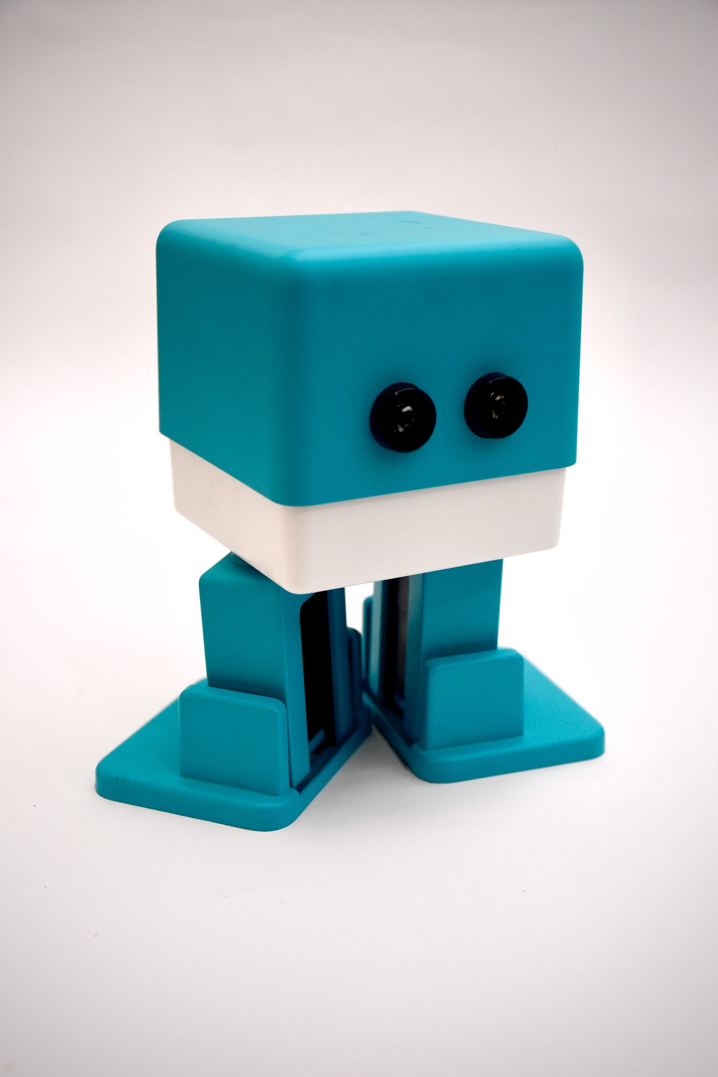 A picture pf a turquoise and white plastic bot with two black eyes against a black background.