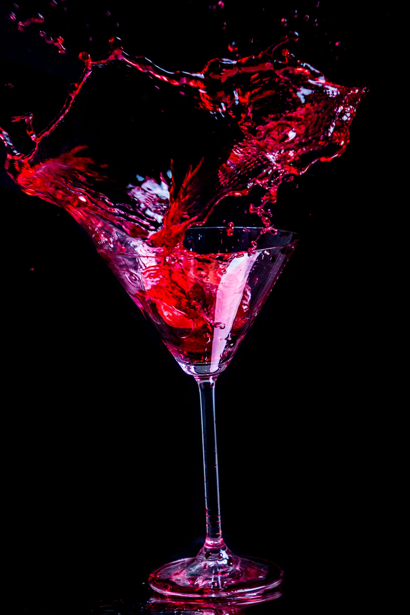 Red alcohol spills out of a V-shaped clear stem glass, as if the glass were being shaken.