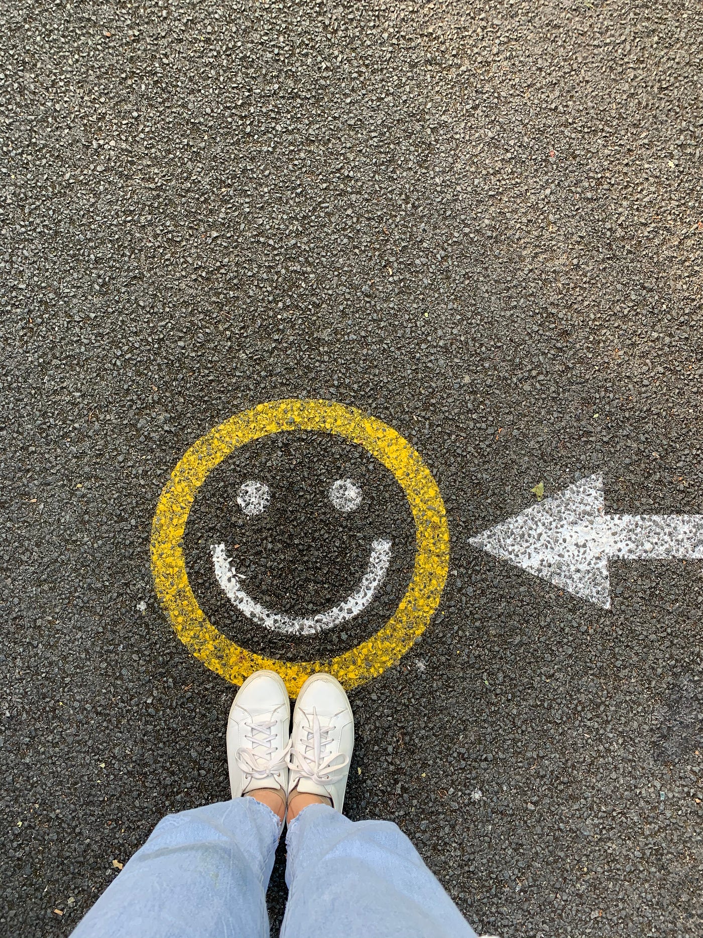 feet standing on a chalk smiley face on asphalt road