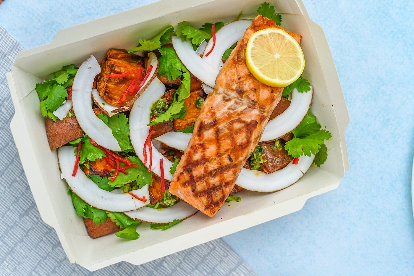 A plate of healthy food, including a strip of salmon with a lemon atop it. The salmon strip perches on a bed of lettuce and other vegetables.
