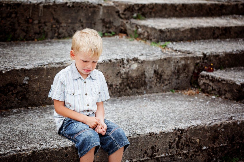 Little Boy crying, sitting on stone steps in the park. Loneliness, melancholy, stress