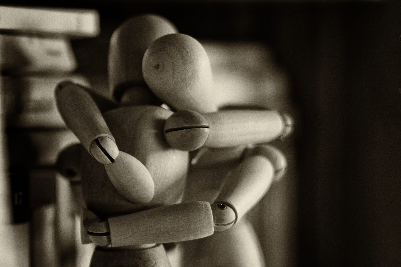 Sepia toned image of two wooden artist’s mannequins wrapped in an embrace